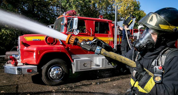 fire fighter in uniform holding fire hose standing next to a fire truck