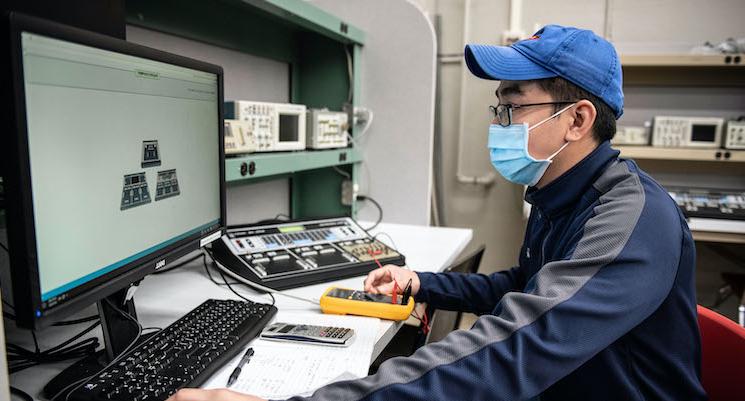 male student testing electronics functionality with tools and computer