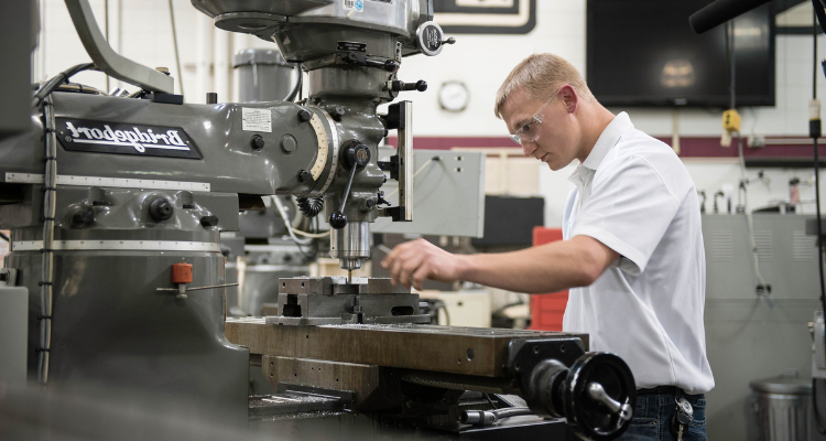 male student working on a drill press and setting up for production