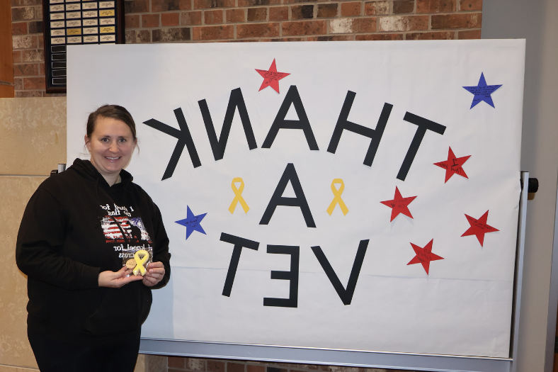 Anna Reiman posed in front of a board reading Thank a Vet with a cookie she made for the event